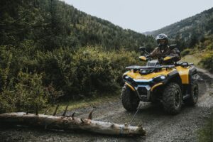 Gelbes ATV Guardian 500 zieht einen großen Baumstamm auf einem Waldweg in bergiger Landschaft