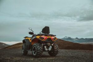 Gelbes ATV Guardian 500 mit Rücksitz auf unbefestigtem Gelände vor Bergen und bewölktem Himmel