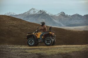 Person fährt gelbes ATV Modell Guardian 500 auf bergigem Gelände mit schneebedeckten Gipfeln